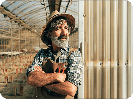 Older farmer in overalls standing outside a greenhouse